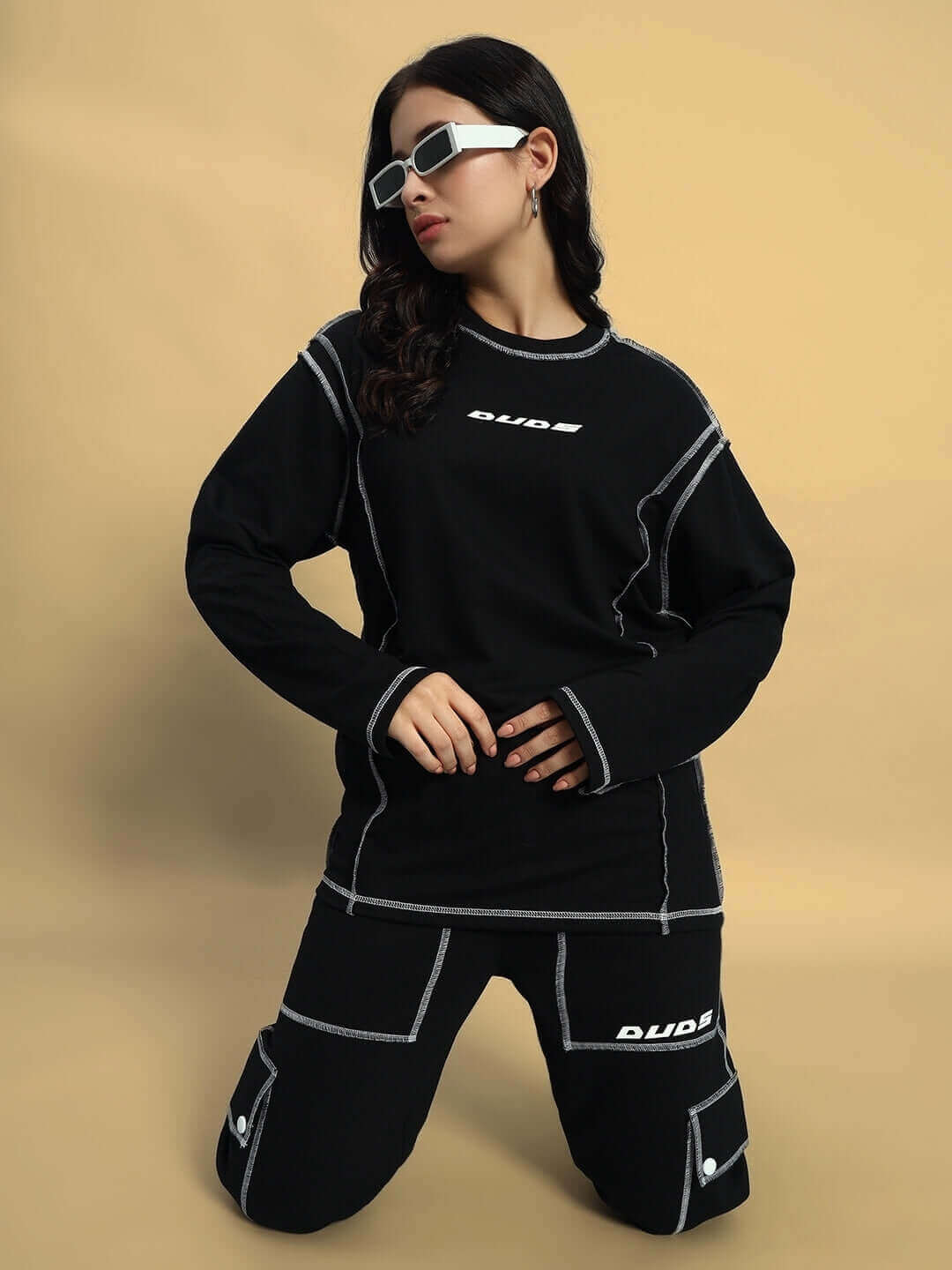 Model wearing women's dynamic oversized black sweatshirt with contrast stitching, paired with matching pants, showcasing modern fashion.