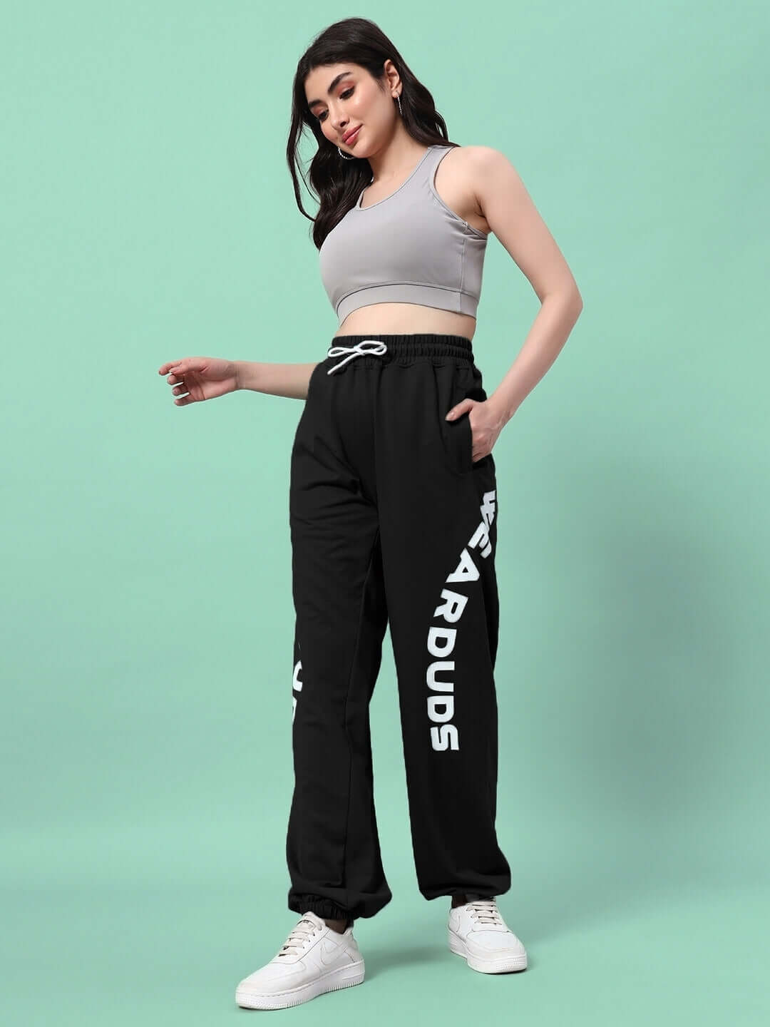 Woman wearing WOMEN'S ELLEN RELAXED FIT JOGGER BLACK with white sneakers, standing against a teal background.