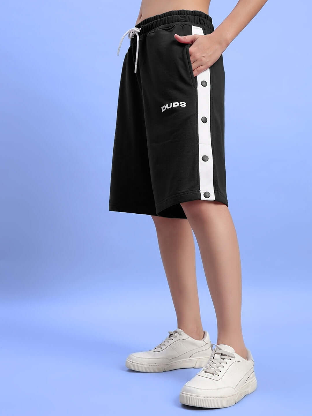 Women's black Ezel regular fit shorts with white side buttons, worn with white sneakers on a light blue background.