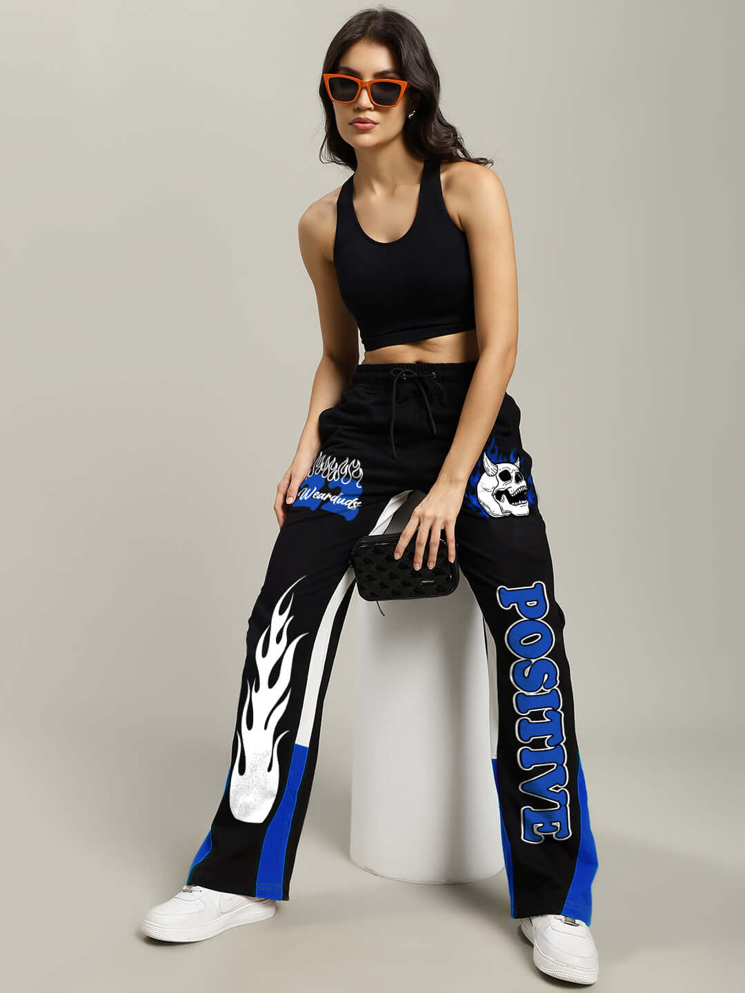 Stylish woman wearing WOMEN'S FEARLESS POSITIVE RELAXED FIT JOGGERS BLACK-BLUE, highlighting bold side panels and "Positive" text.