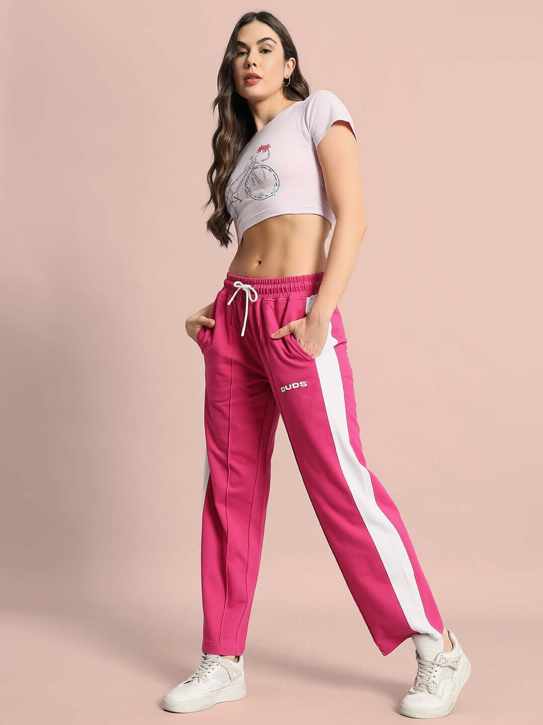 Model wearing Women's Feeling Chipper Crop-Top in Lilac, paired with vibrant pink and white track pants, highlighting casual style.