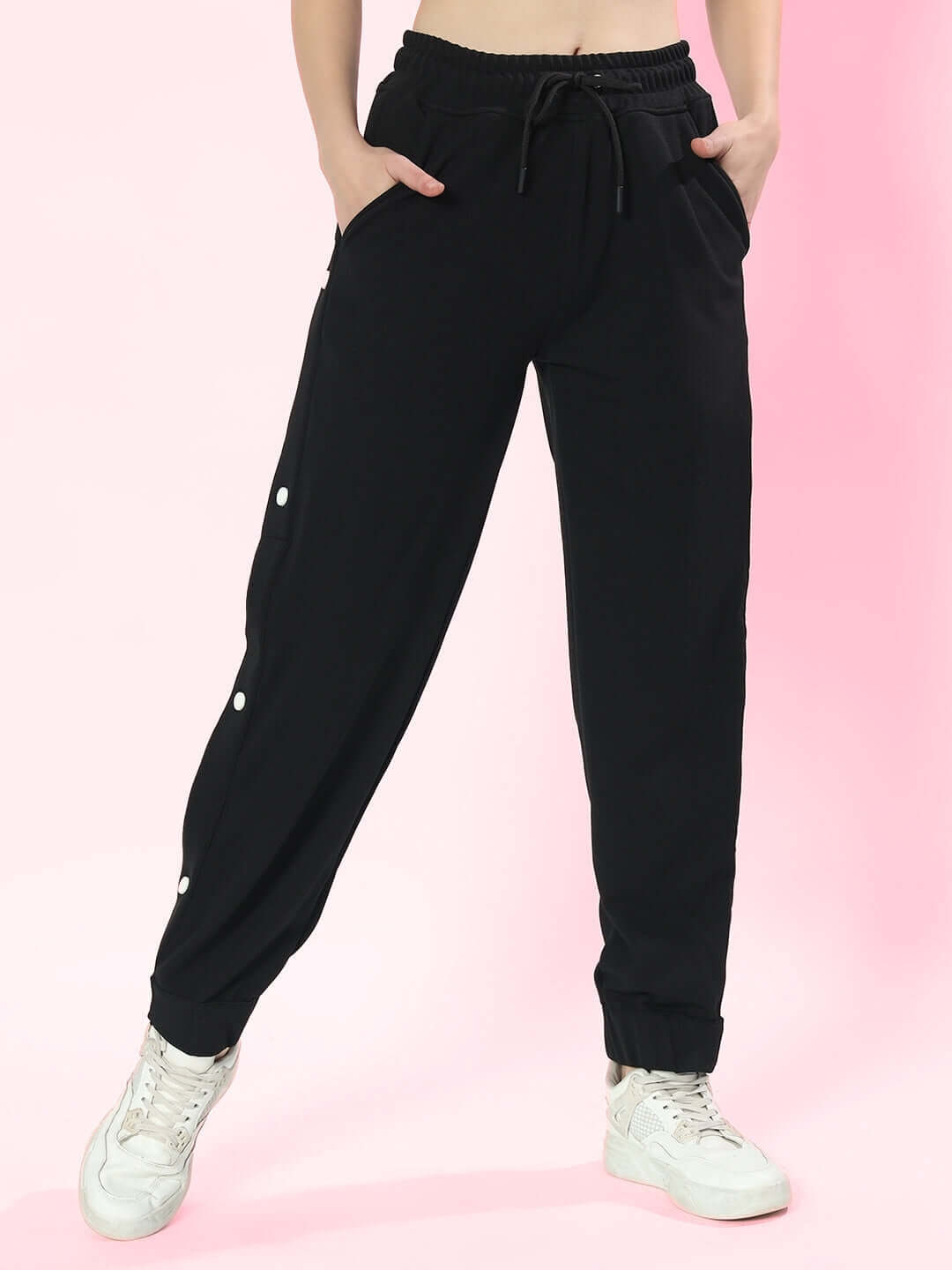 Women's hip hop joggers in black with drawstring waist, styled with white sneakers, on a pink background.