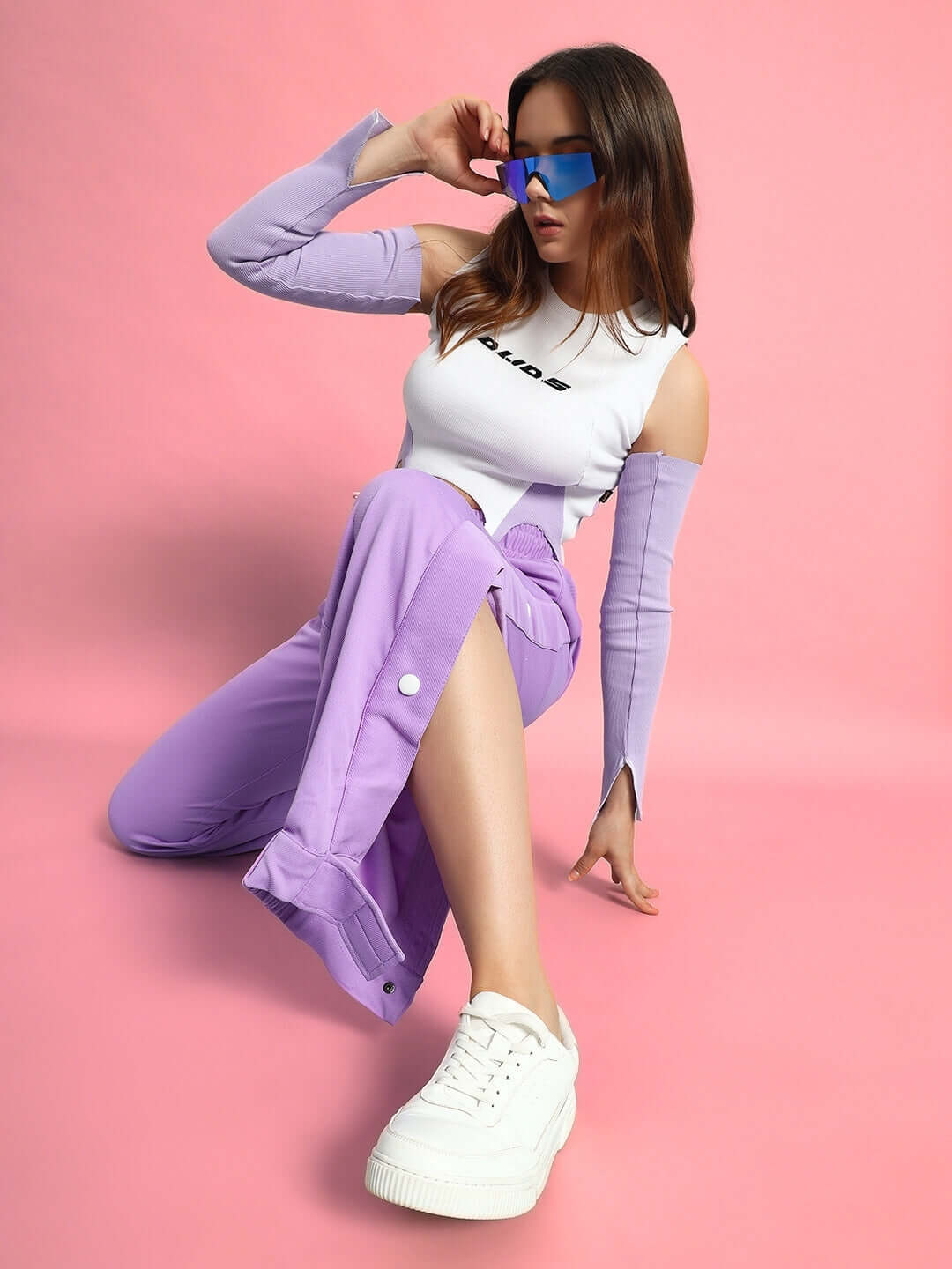 Model wearing lavender women's hip hop joggers and white sneakers against a pink background, showcasing stylish streetwear fashion.