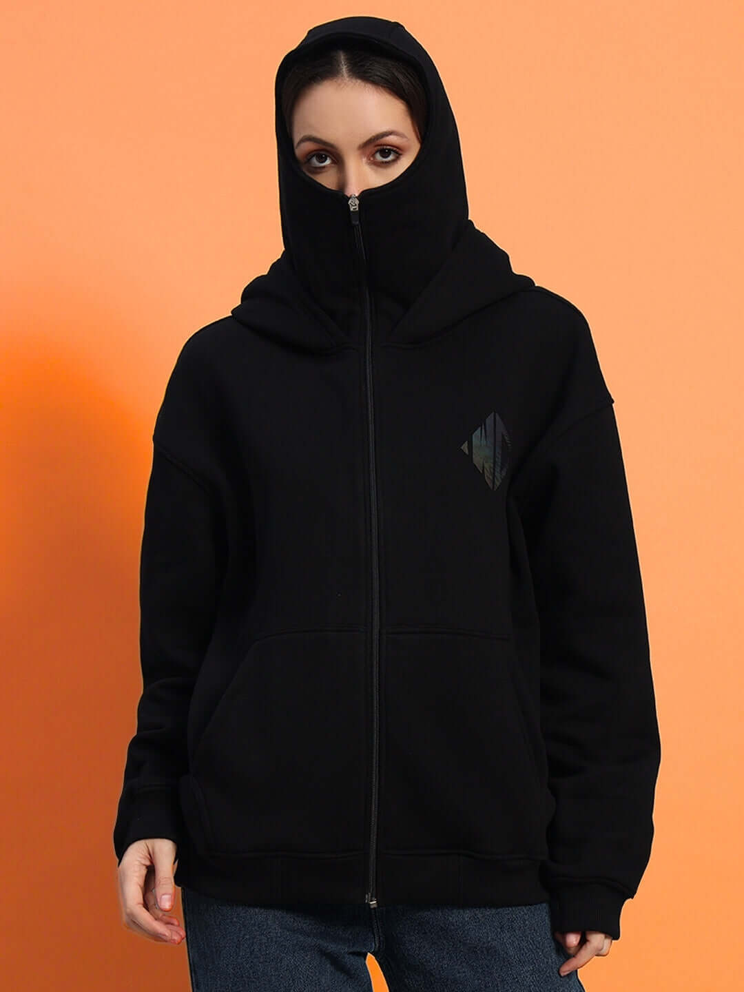 Woman wearing WOMEN'S MARKSMAN OVERSIZED FLEECE HOODIE BLACK, showcasing the cozy and stylish oversized silhouette against an orange background.