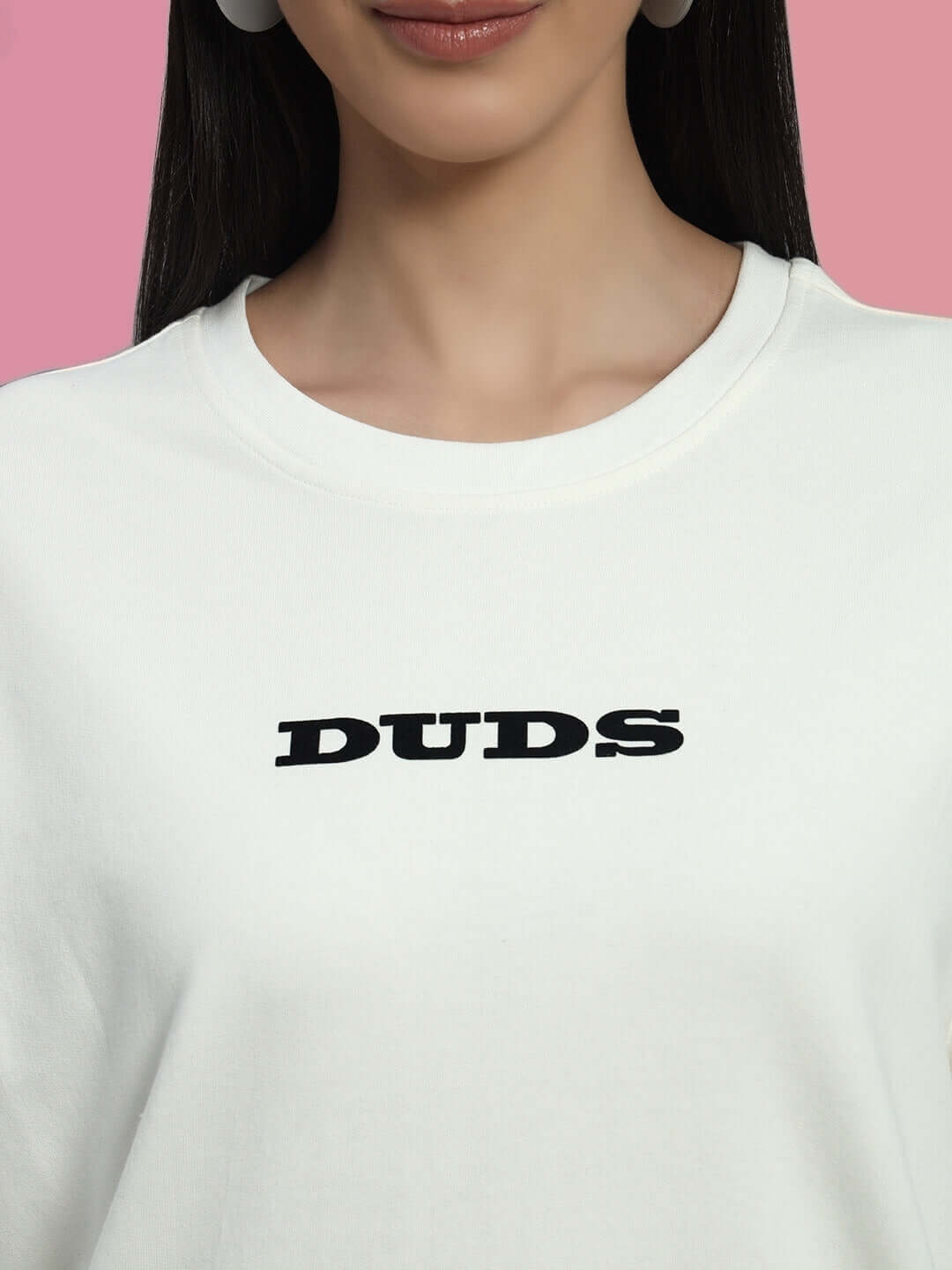 Close-up of a woman wearing an off-white cotton co-ord set with 'DUDS' text, featuring a relaxed fit and crew neck under soft pink background.