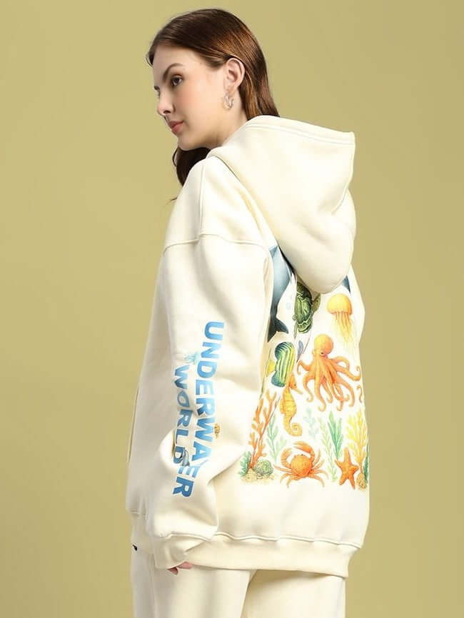 Woman wearing WOMEN OCEAN BUDDIES OVERSIZED FLEECE HOODIE OFF-WHITE with ocean-themed design, side view.