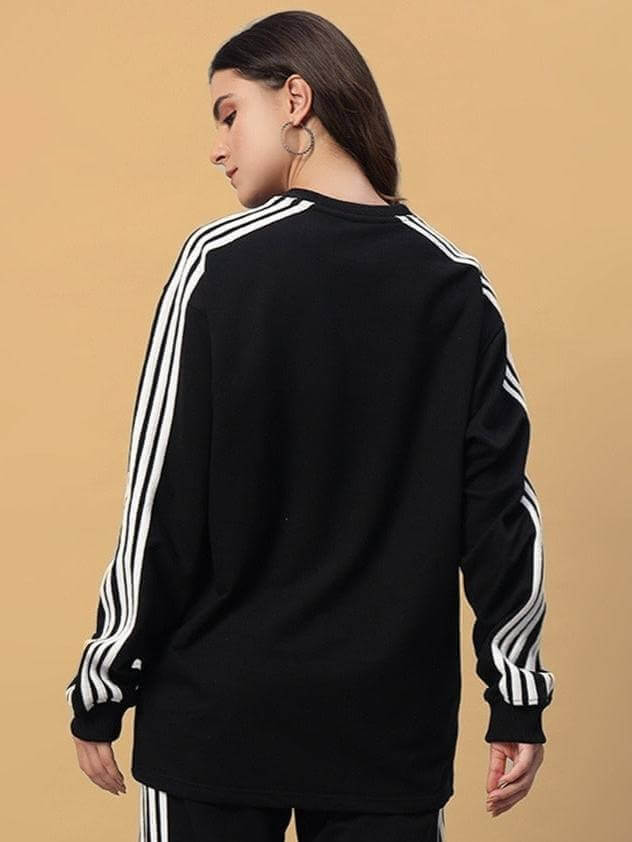 Back view of woman wearing black oversized parka sweatshirt with striped sleeves, made from premium cotton fabric.