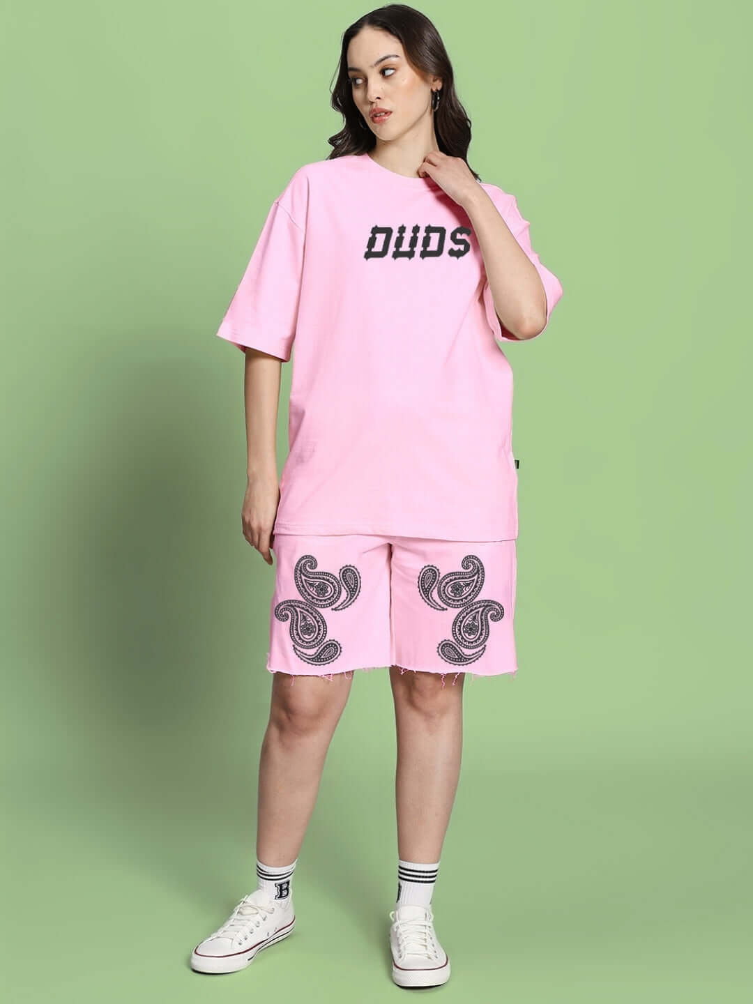 Woman wearing WOMEN'S MESSI PAISLEY PRINT CO-ORD SET PINK with oversized paisley print t-shirt and shorts on a green background.