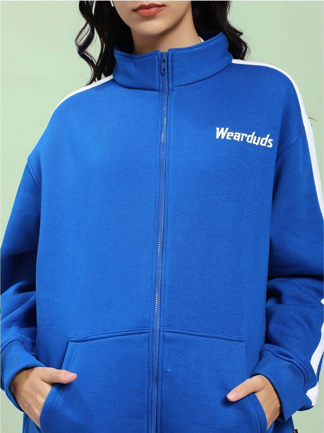Woman wearing WOMEN RAPID STRIDE COTTON FLEECE JACKET ROYAL BLUE with zip and white side stripes, showcasing sporty chic.