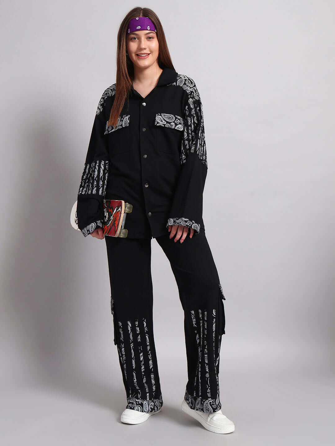 Woman wearing black Sanganeri joggers with custom fit option and traditional designs, holding a skateboard, standing on a gray background.