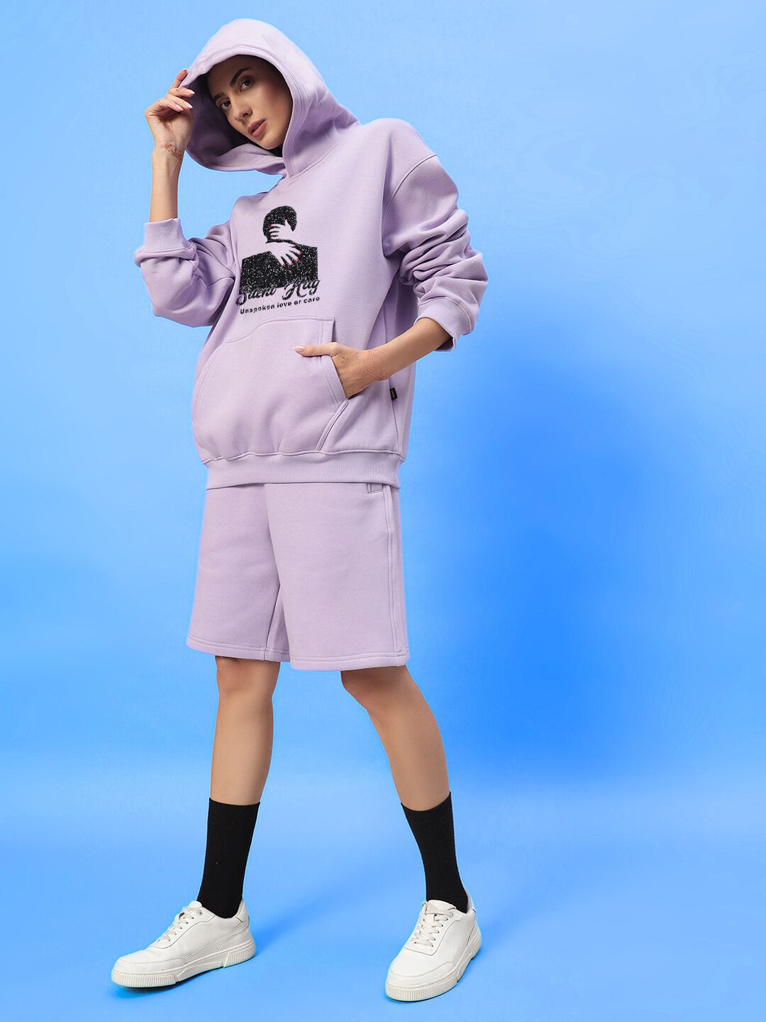 Woman wearing WOMENS SILENT HUG PRINTED FLEECE CO-ORD LILAC with hoodie and shorts, standing in front of blue background.