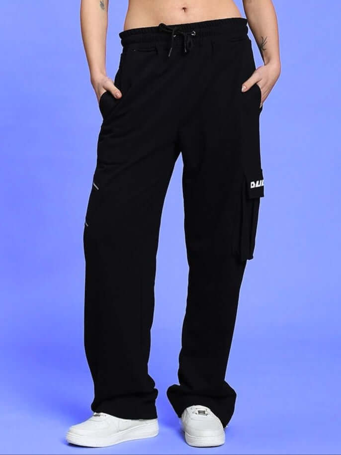 Woman wearing black women's Skidder cargo pant with pockets, paired with white sneakers, on a blue background.
