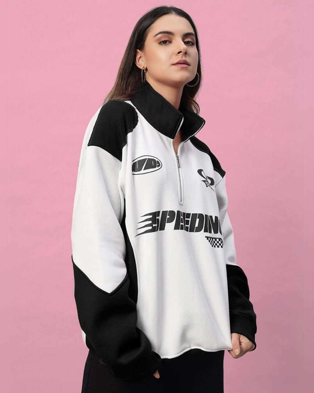 Woman wearing a black and white colorblock jacket with "Speeding" print, against a pink background.