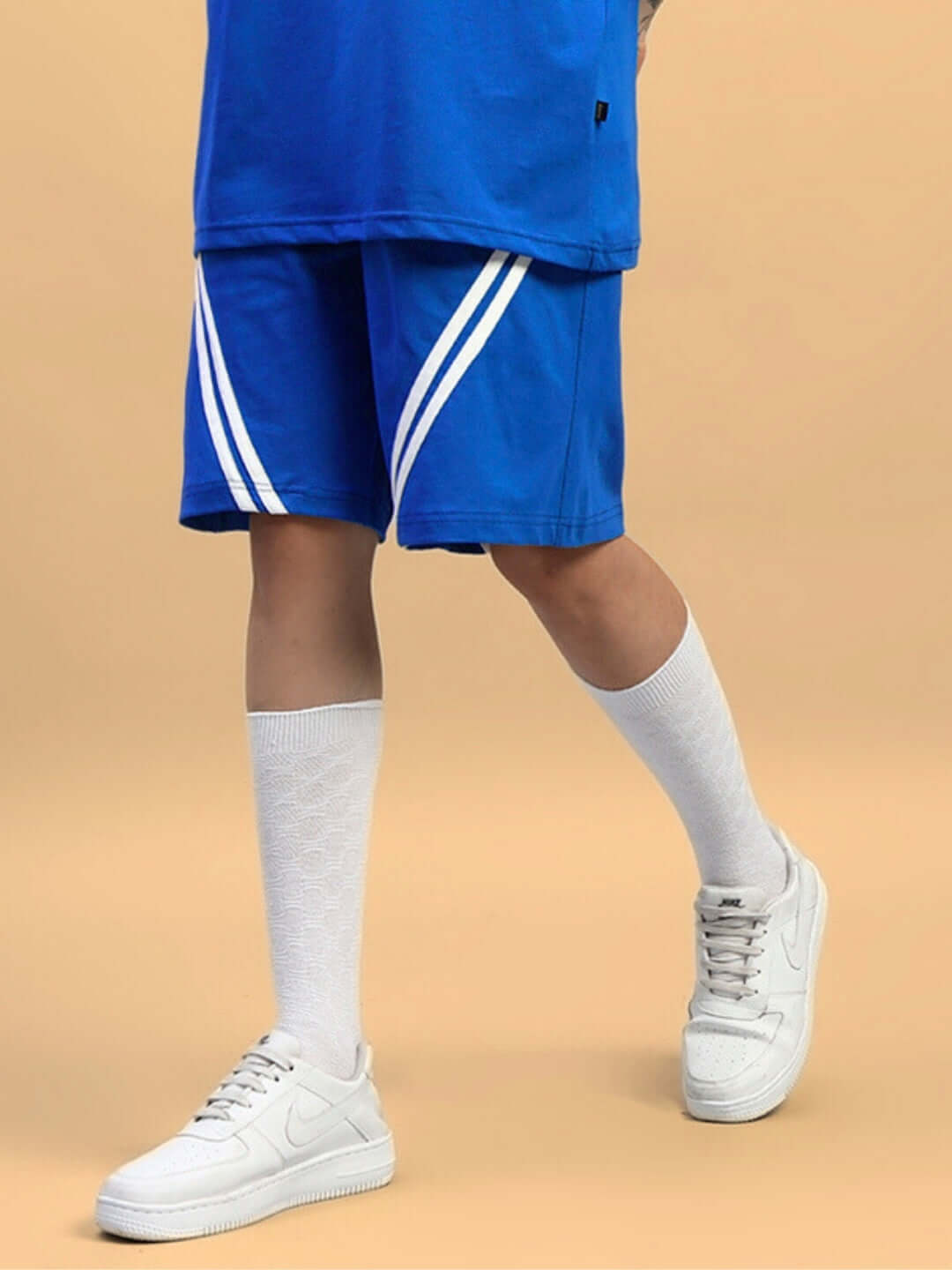 Model wearing blue star jumper shorts with white stripes, paired with white socks and sneakers, showcasing casual fashion style.