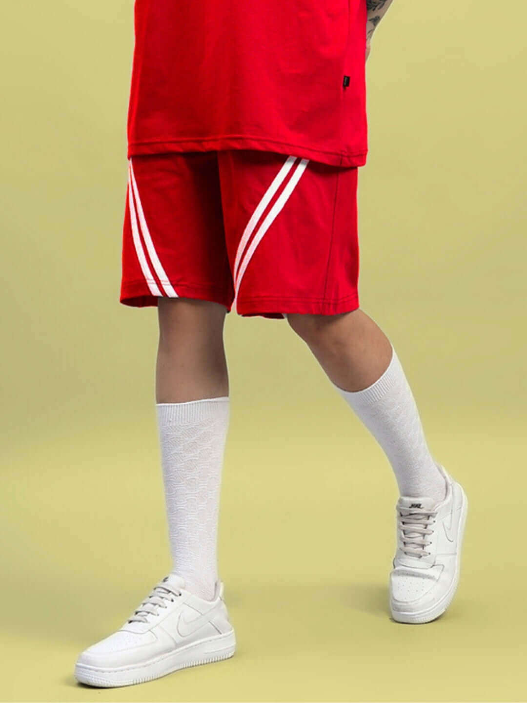 Women's red star jumper shorts with white stripes, regular fit, paired with white socks and sneakers on a light yellow background.