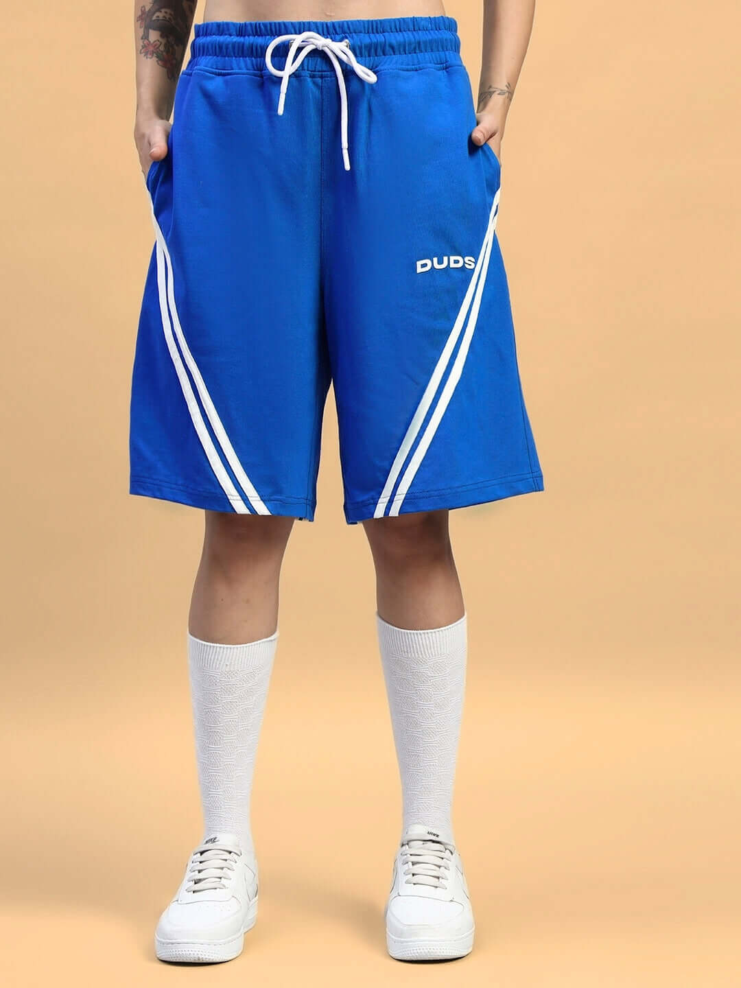 Model wearing blue shorts with white stripes and 'DUDS' text, styled with knee-high socks and sneakers.