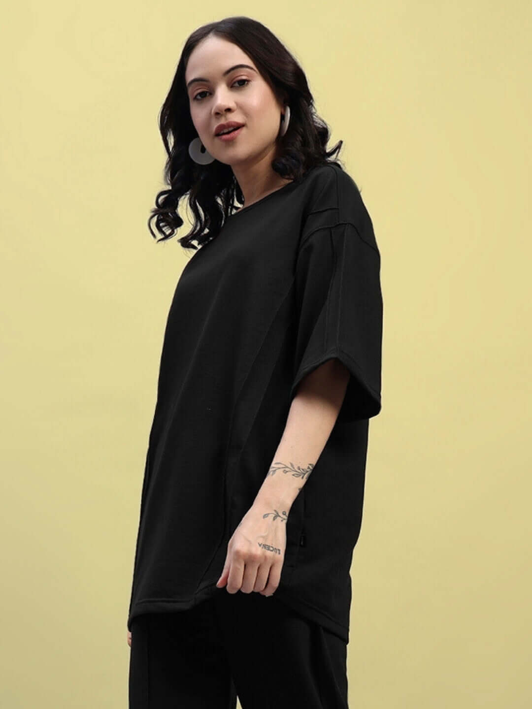 Woman wearing a Women's Superior Oversized Black T-Shirt, made from premium cotton French terry lycra, posing against a yellow background.