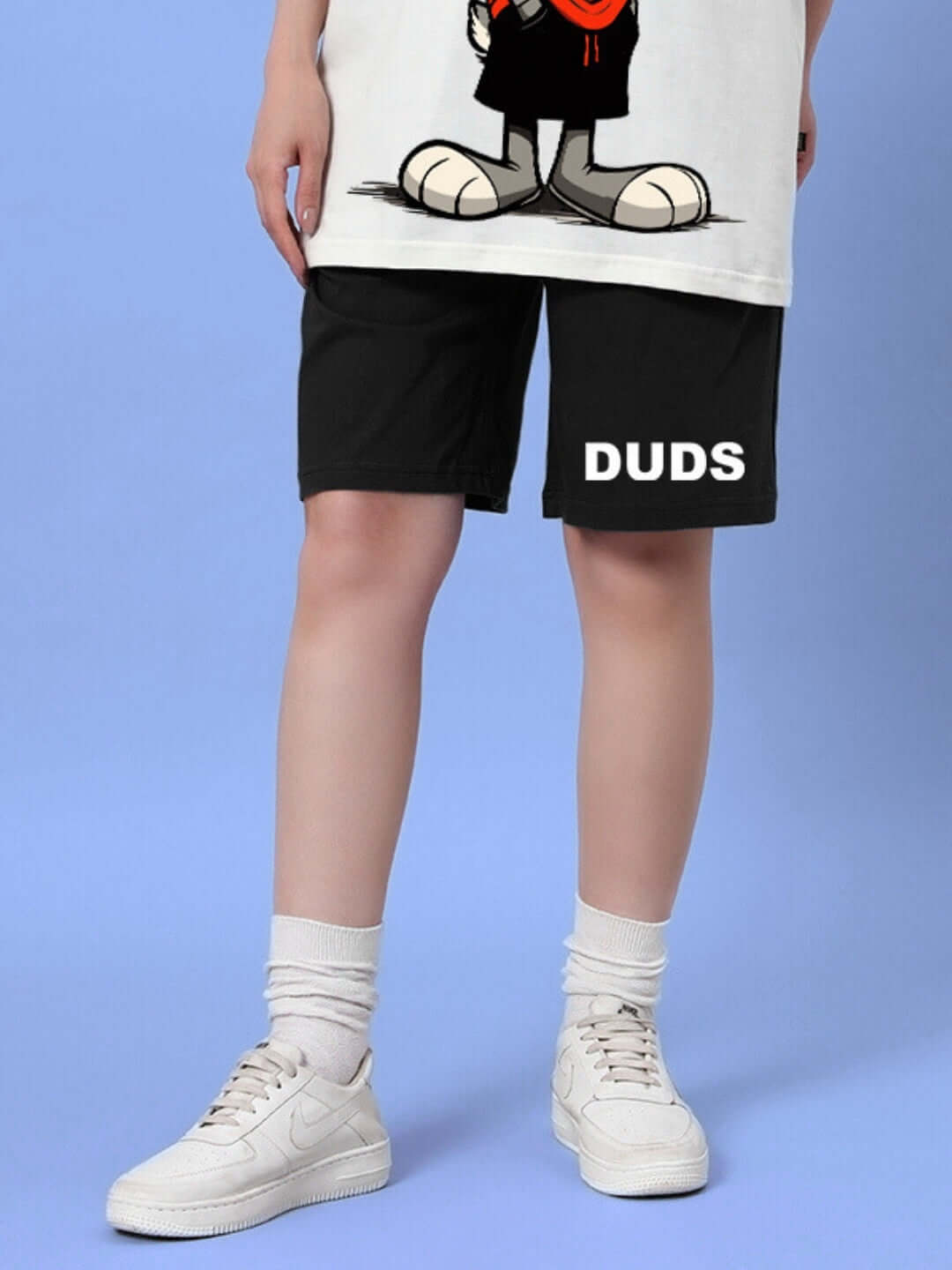 Woman wearing DUDS Think Big black summer shorts with custom fit option, white sneakers, and socks, standing against a blue background.
