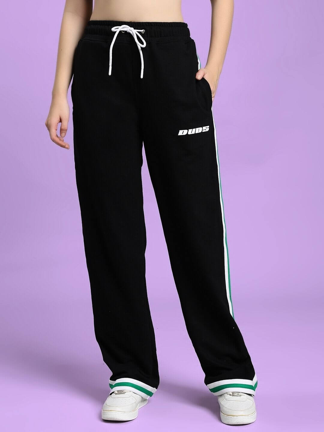 Person wearing WOMEN'S VELO GREEN STRIPE RELAXED FIT JOGGER BLACK with green side stripe on purple background.