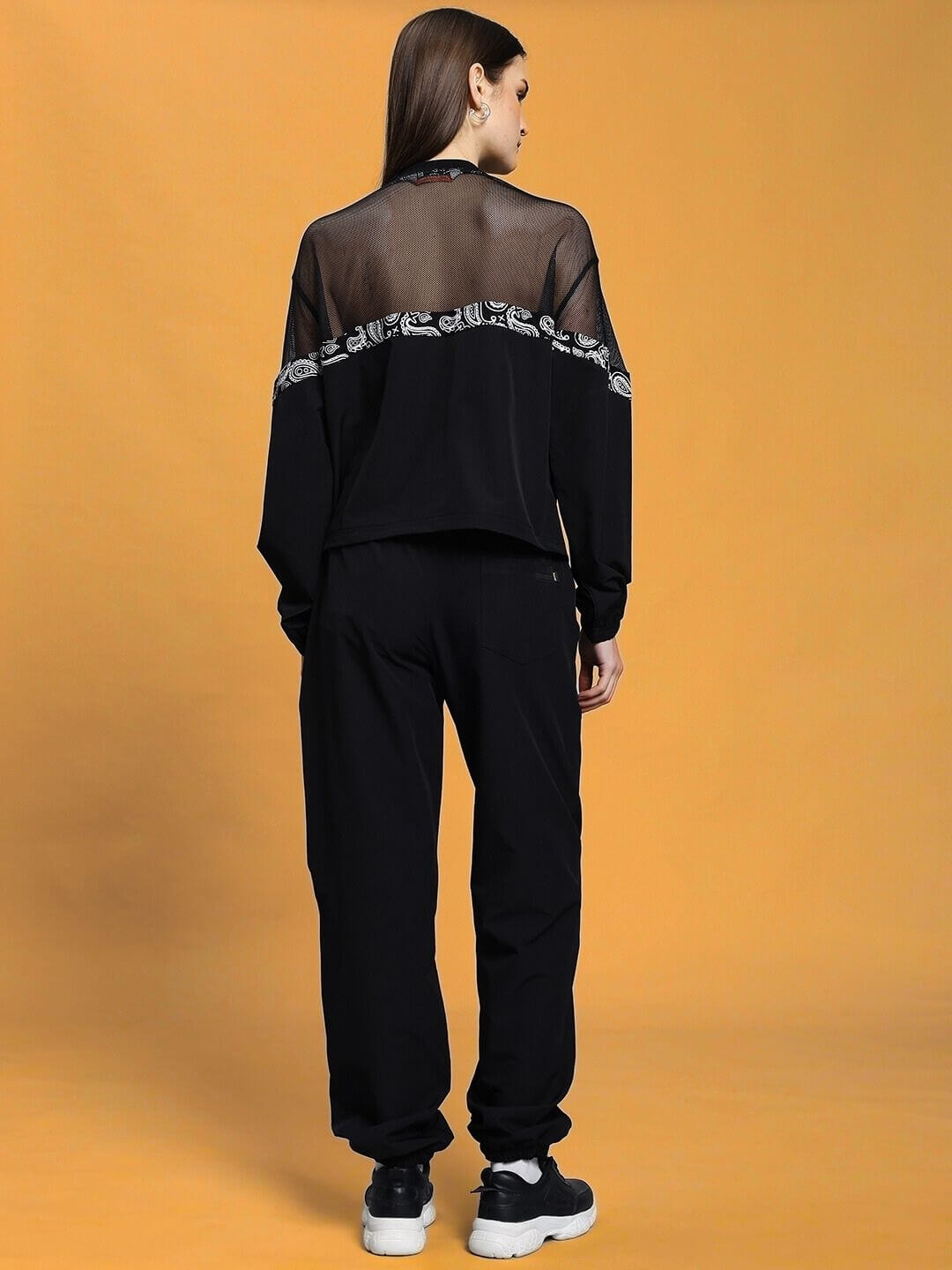 Back view of woman's relaxed fit black co-ord set with mesh panel, unisex design, and elasticated waistband. Polyester fabric.