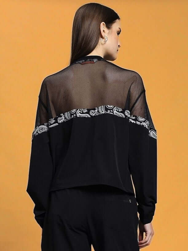 Back view of WOMEN'S YESMIN RELAXED FIT TOP BLACK showcasing sheer and patterned details on a model against an orange background.