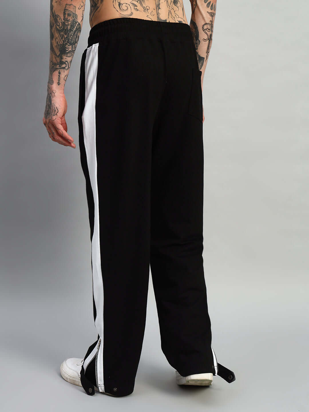 Back view of black-white Wonder Slit Zipper Joggers, featuring white side stripes and an elastic waistband, modeled by tattooed individual.