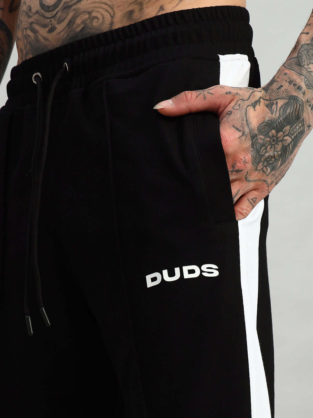 Close-up of black-white Wonder Slit Zipper Joggers by DUDS, showcasing stylish design and tattooed hand detail.