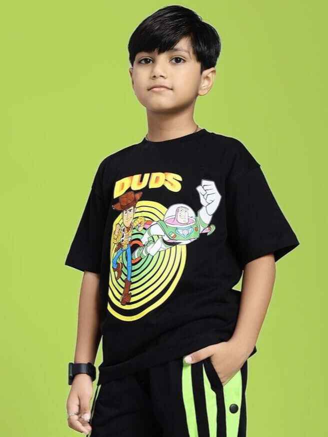 Child wearing WOODY BUZZ T-SHIRT FOR BOYS AND GIRLS BLACK with cartoon graphic design on green background.