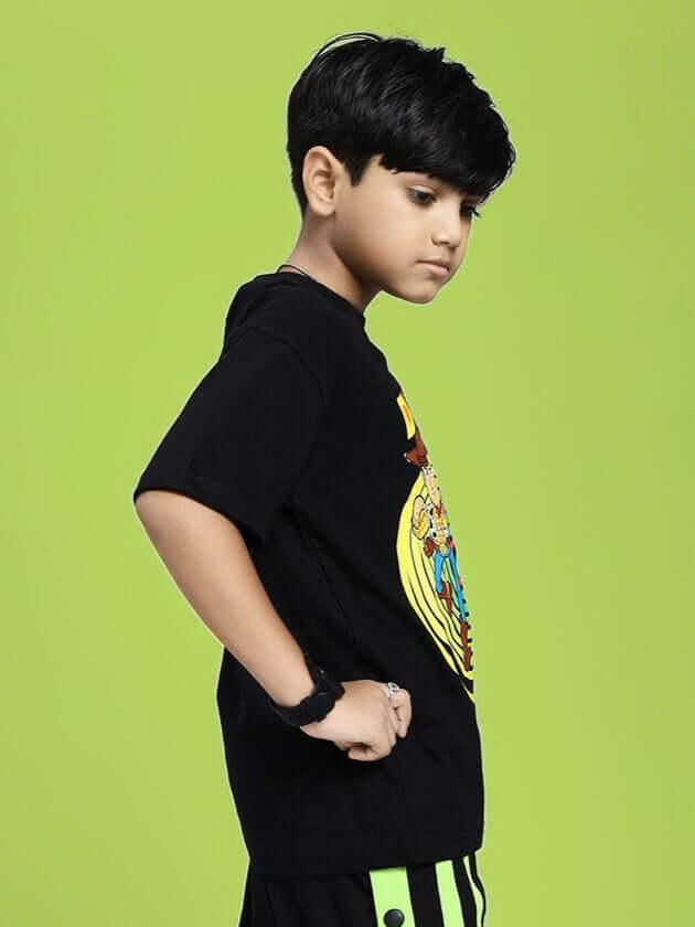 Child wearing WOODY BUZZ T-SHIRT FOR BOYS AND GIRLS BLACK with character graphic, side view on green background