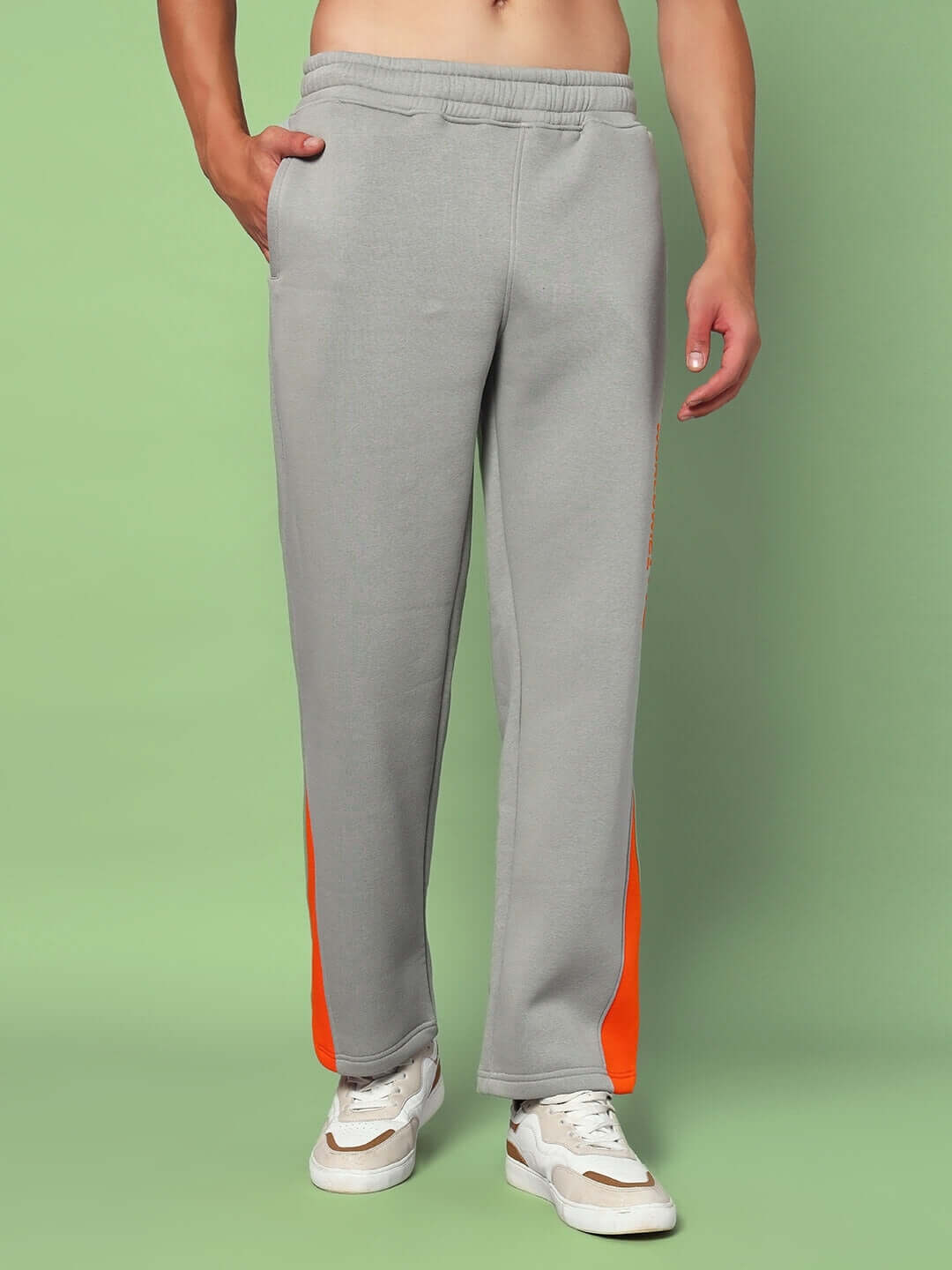 Model wearing WORLDWIDE FLEECE COLORBLOCK CO-ORD GREY pants with orange accents, showcasing streetwear style against a green background.