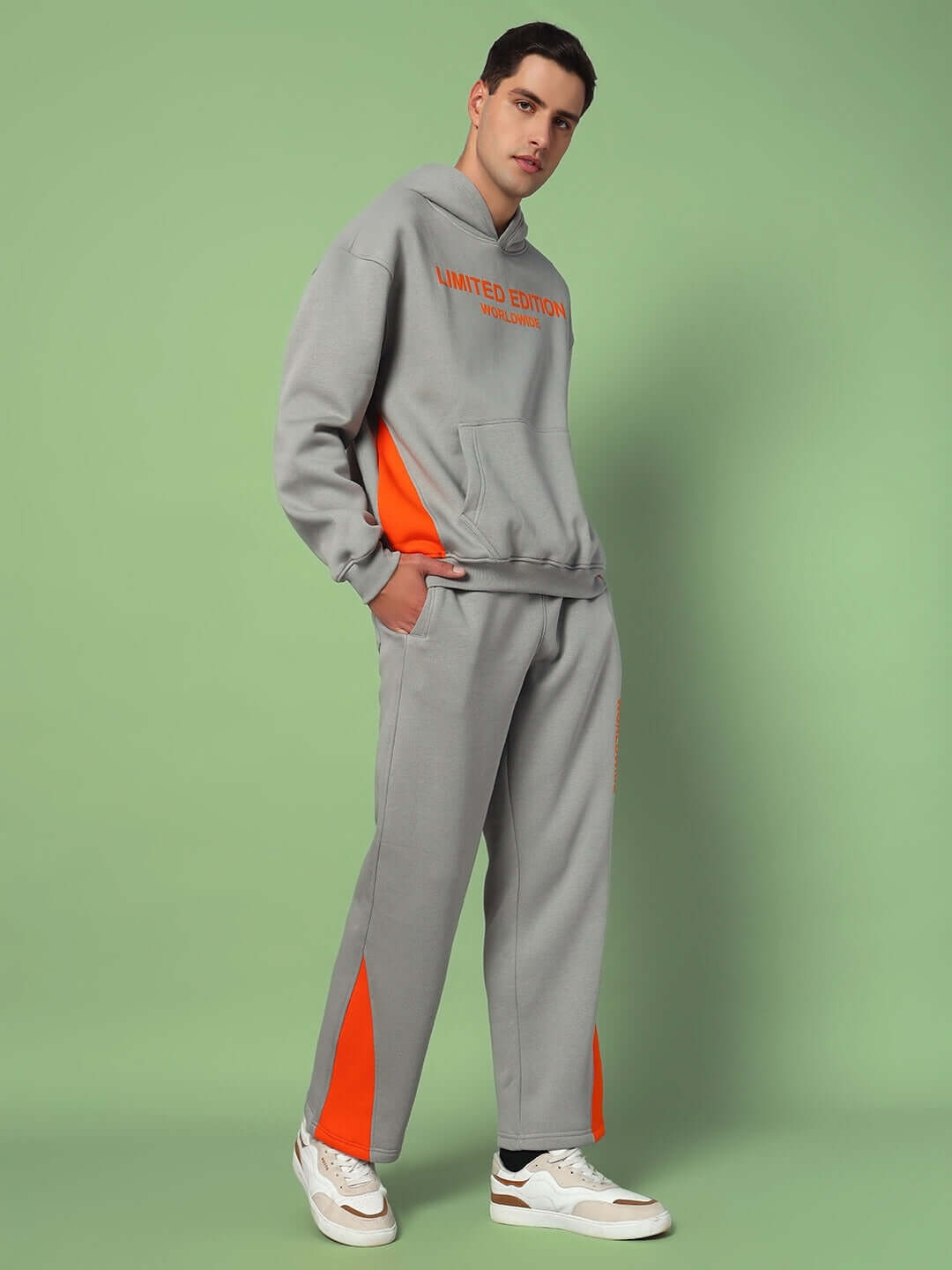 Alt Tag: Model wearing WORLDWIDE FLEECE COLORBLOCK CO-ORD GREY, featuring a modern grey and orange colorblock design, standing on green backdrop.