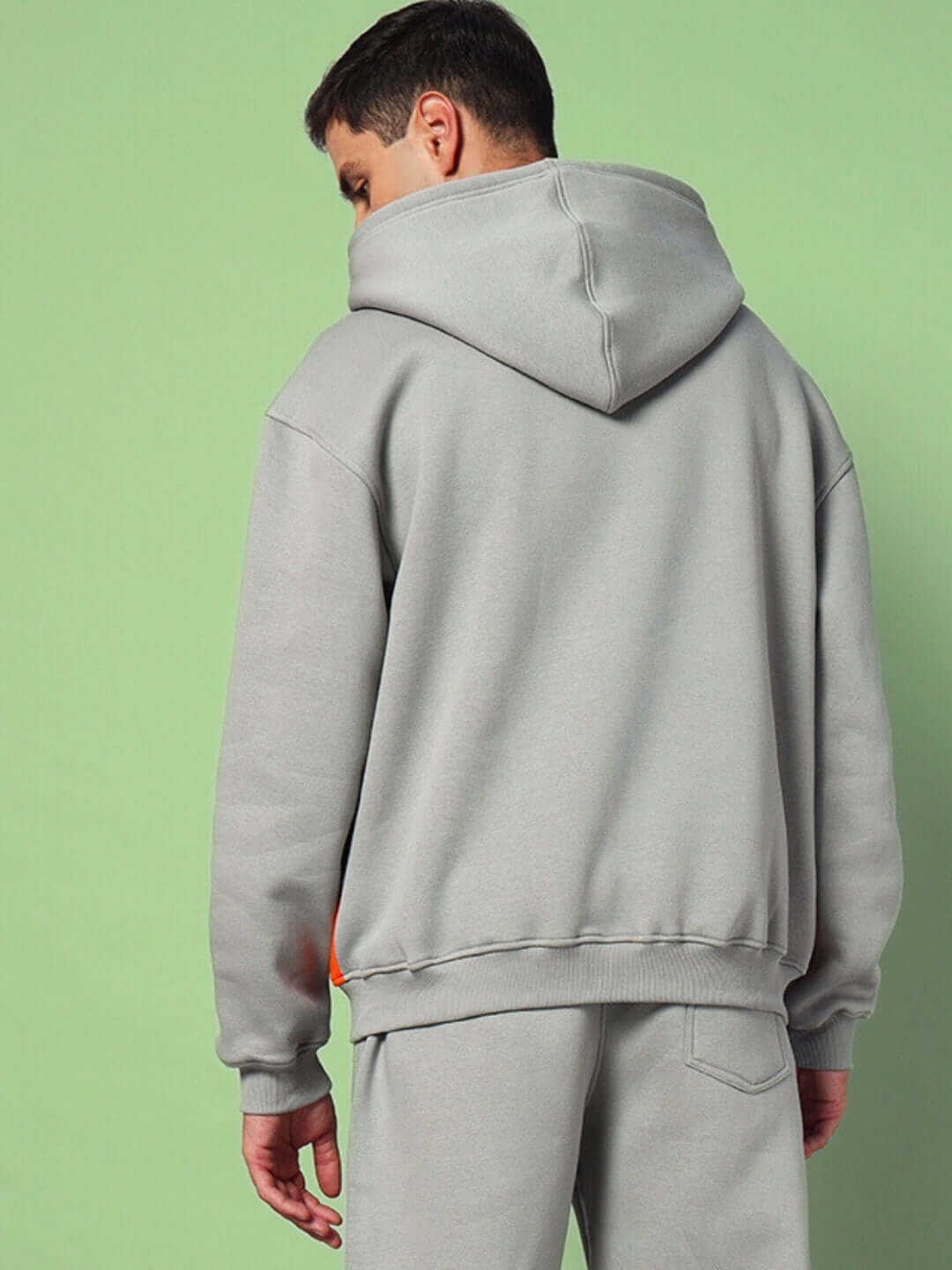 Man wearing WORLDWIDE FLEECE COLORBLOCK CO-ORD GREY showing back view with hood up against a green backdrop.