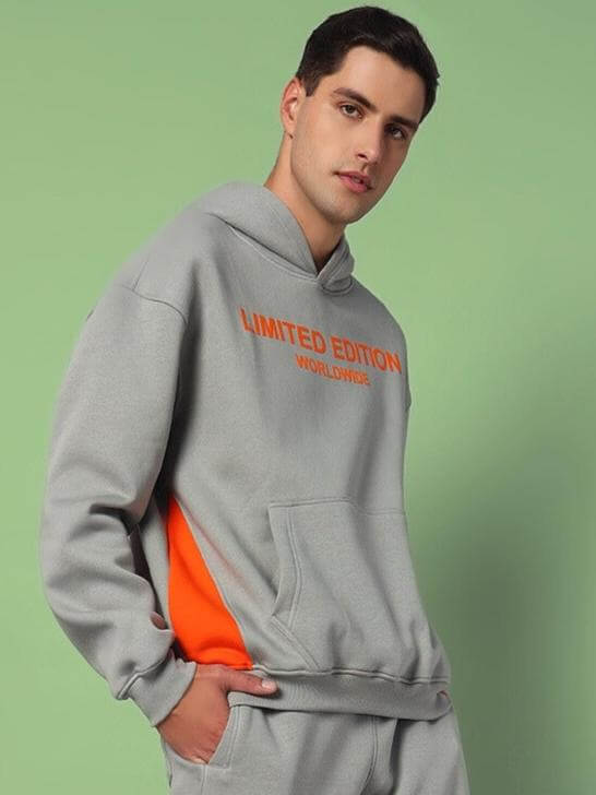 Man wearing a grey WORLDWIDE COTTON FLEECE HOODIE with limited edition print, featuring an orange accent and kangaroo pocket.