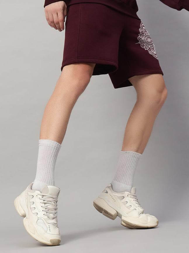 Person wearing WEARDUDS YANTRA FLEECE SHORTS WINE showcasing a casual sporty look with white sneakers and socks.