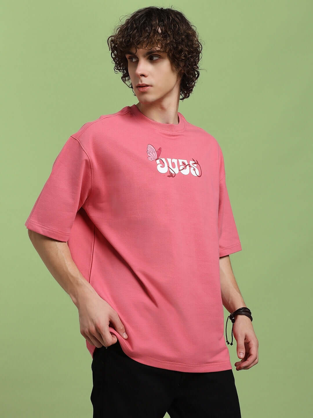 Man wearing YOUR FEELING PRINTED T-SHIRT PINK with graphic design on front, showcasing modern casual style against a green background.