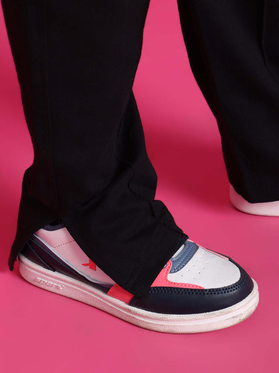 Close-up of pink and black sneakers paired with black pants on a vibrant pink background.