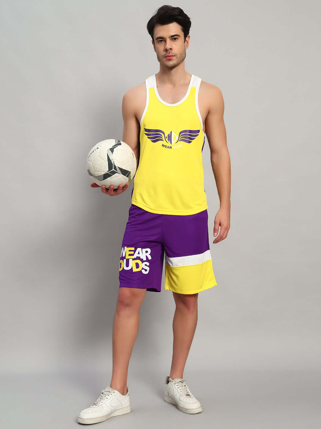Male model wearing ZENITH GYM CO-ORD SET YELLOW-PURPLE holding a soccer ball, showcasing athletic style and performance.
