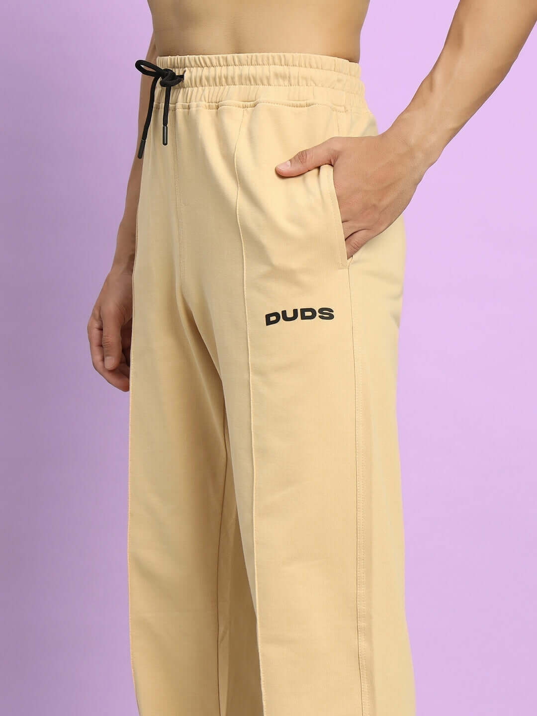 Beige ZION side slit joggers by DUDS with black drawstring and pocket detail, worn by a model on a lavender background.