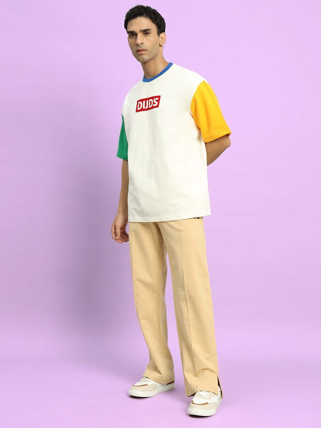 Model wearing ZION Side Slit Joggers in beige, styled with a colorful DUDS t-shirt, showcasing casual fashion on a purple background.