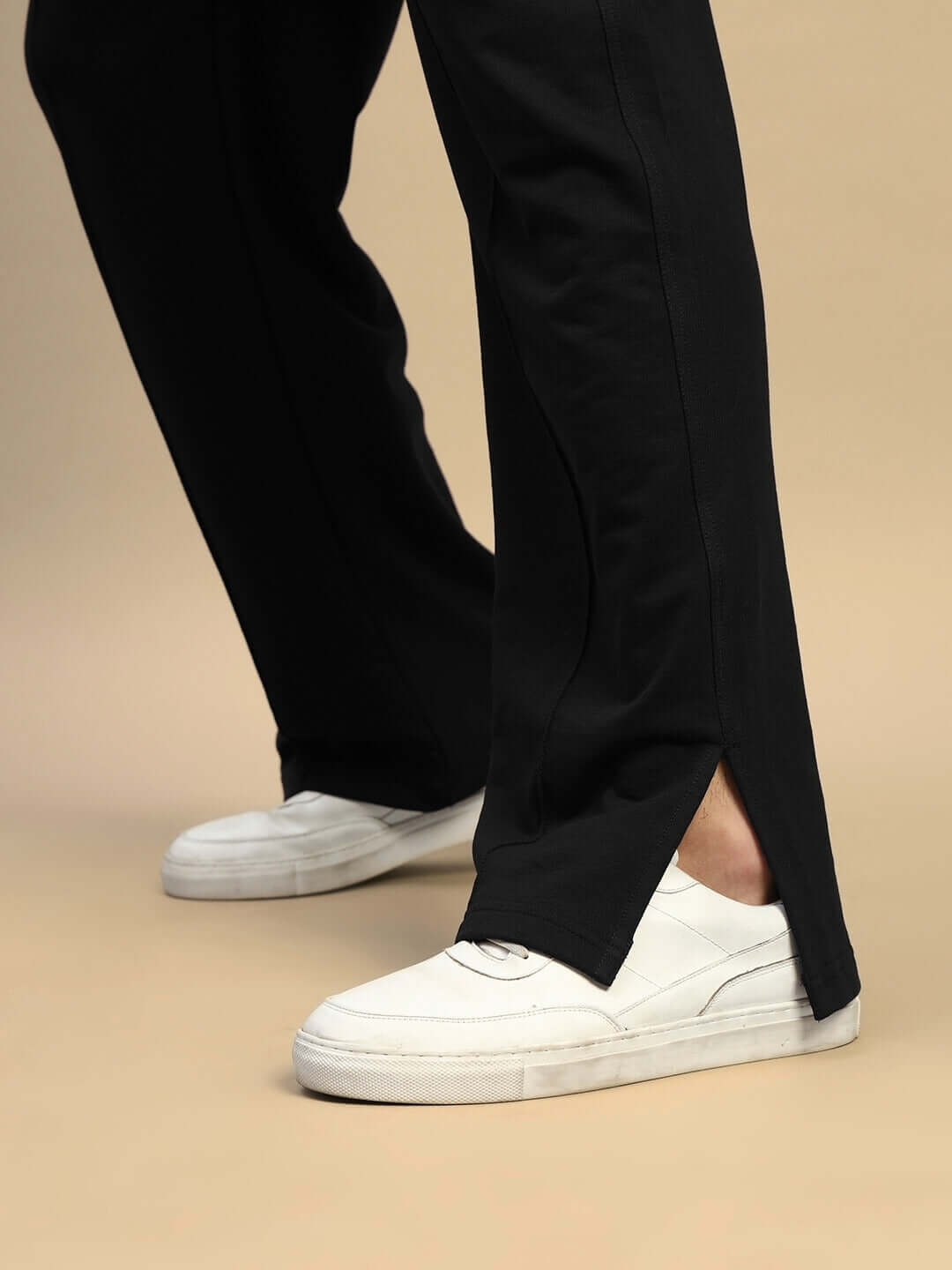 Unisex black joggers with relaxed fit and split hem, paired with white sneakers, showcasing modern casual style and premium fabric.