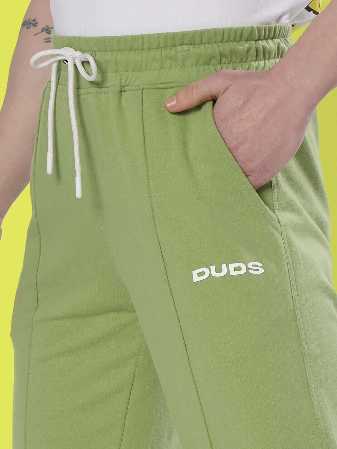 Model wearing ZION Side Slit Joggers in Pista Green with DUDS logo, showcasing drawstring waist and pocket detail.