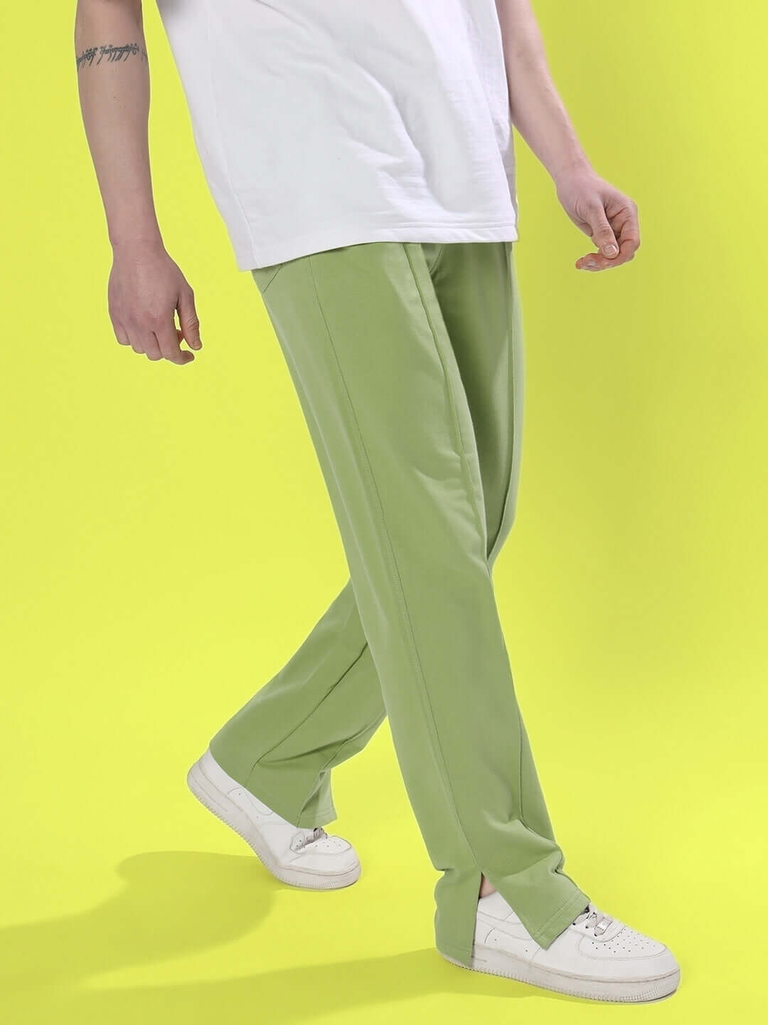 Man wearing Zion Side Slit Joggers in Pista Green with white sneakers against yellow background.