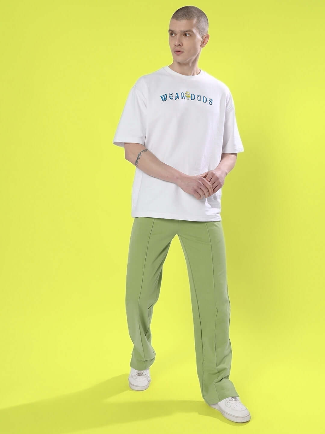 Model wearing ZION Side Slit Joggers in Pista Green with white Duds t-shirt, showcasing casual fashion on a vibrant yellow background.