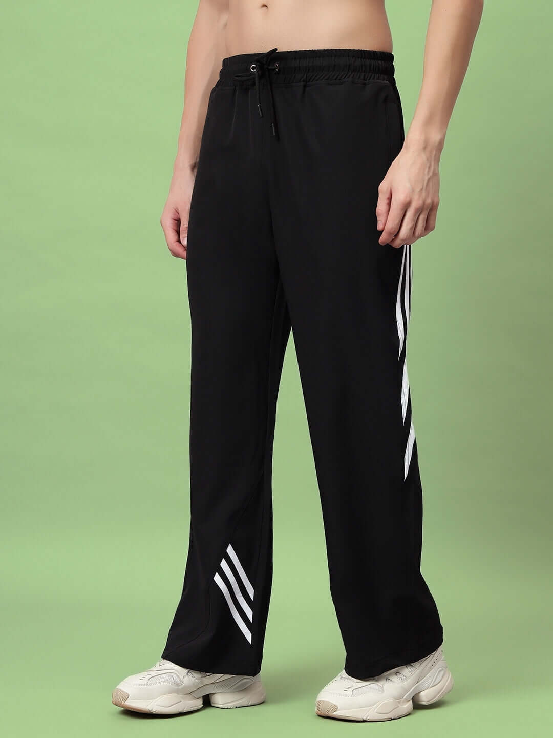 Model wearing black relaxed fit cargo pants with white stripes, featuring spacious pockets and adjustable waist against a green background.