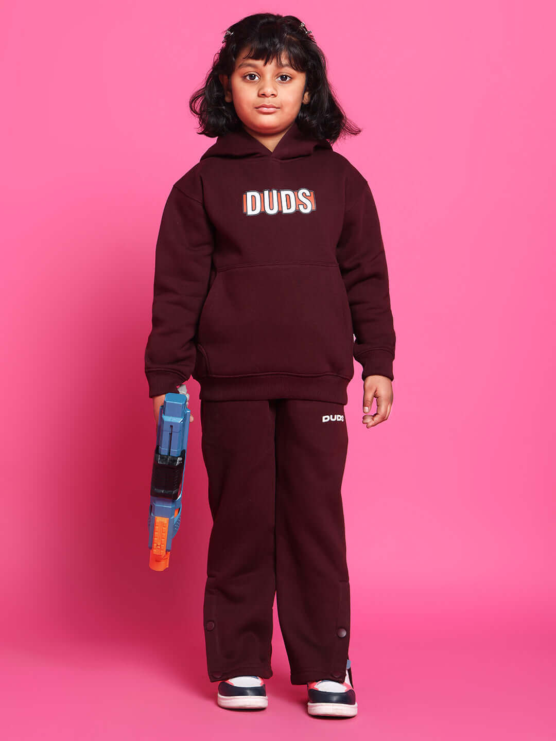 Child wearing Snoopy Fleece Pant in wine color, holding a toy, standing against a pink background. Cozy and stylish kids' clothing.