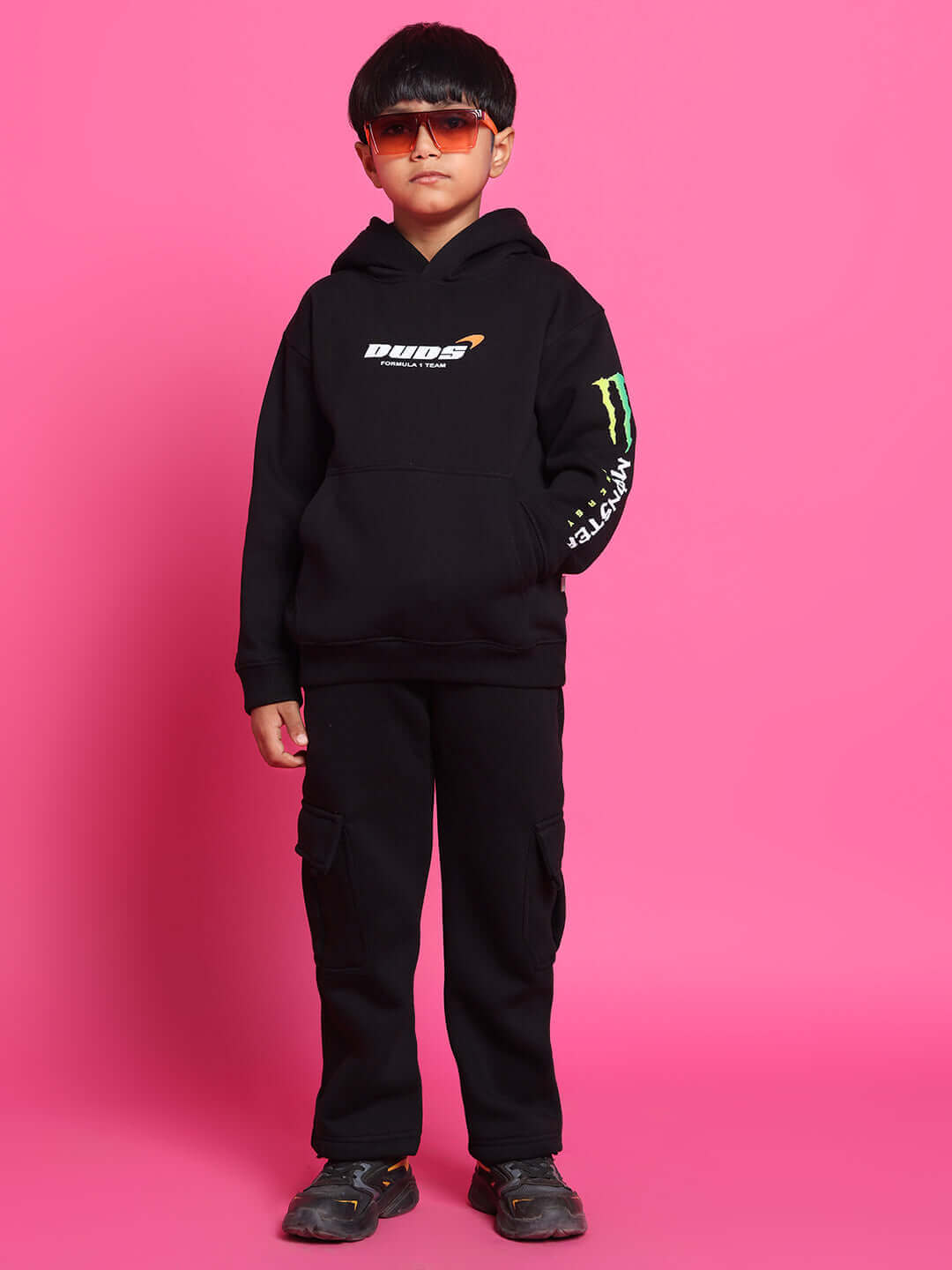 Child wearing black Monster Co-ord hoodie and pants against a pink backdrop, featuring colorful logo graphics, suitable for boys and girls.