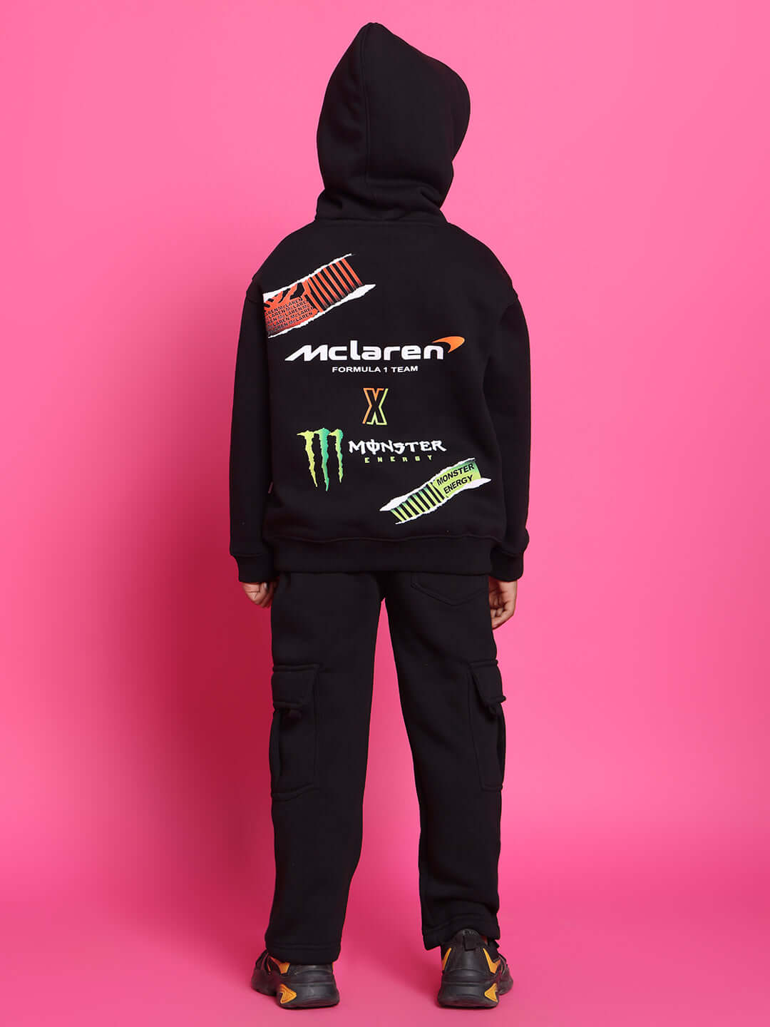 Child wearing black Monster co-ord set with colorful logos, showcasing a hoodie and pants on a pink background.