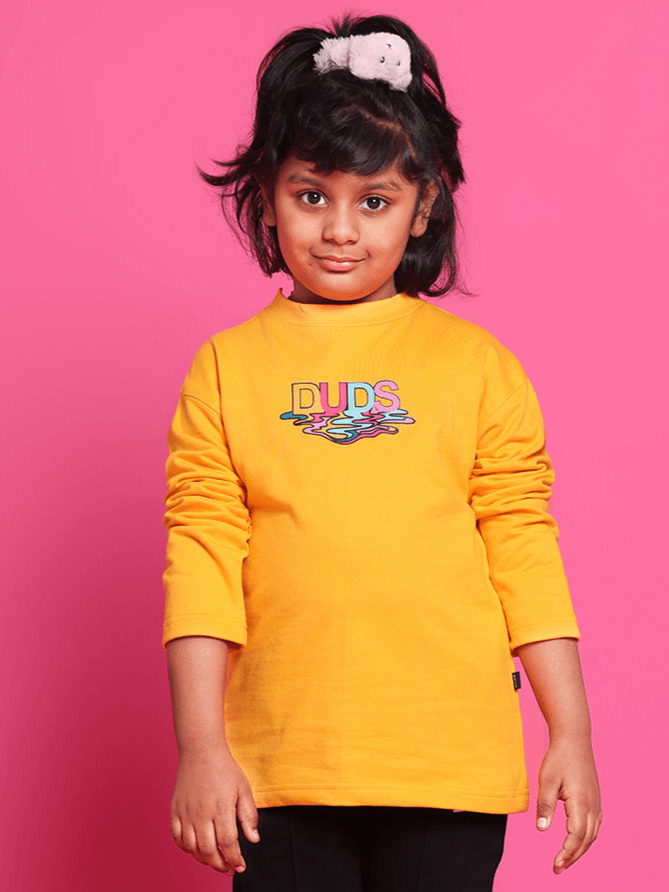 Child wearing yellow oversized sweatshirt with DUDS logo, standing against pink background, showcasing vibrant youth fashion.