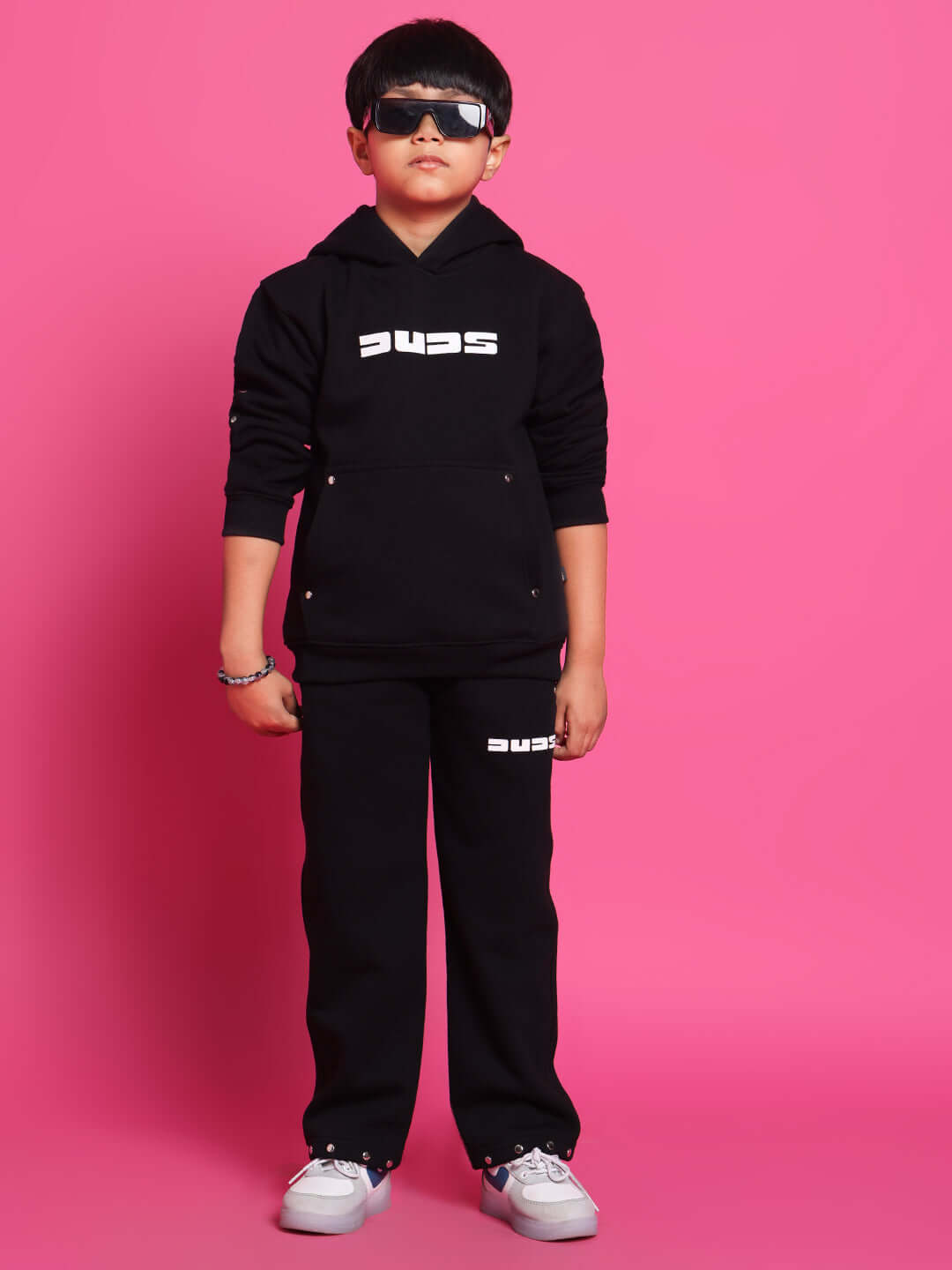 Young boy wearing a black SHOOTER CO-ORD set from DUDS, featuring a hoodie and pants with logo, ideal for both boys and girls.