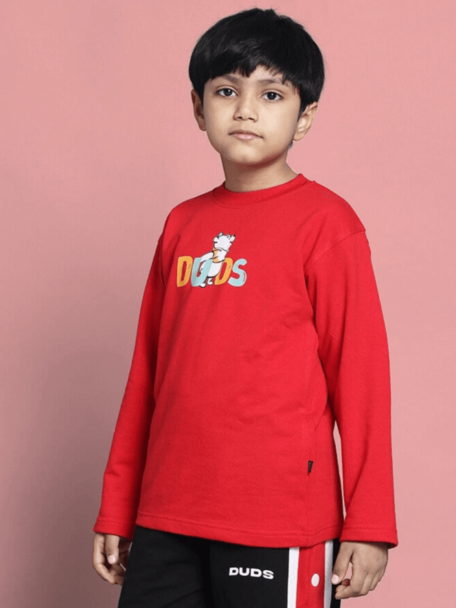 Child wearing red Winnie oversized sweatshirt from DUDS, perfect for boys and girls, standing against a pink background.